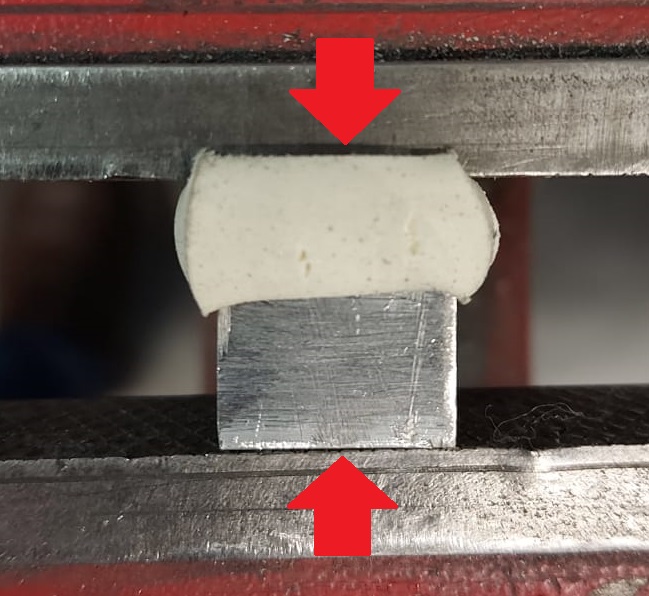Dois blocos com as mesmas dimensões, um de borracha e o outro de alumínio, sendo prensados empilhados em uma morsa. O de borracha deforma muito mais do que o de alumínio para a mesma tensão.